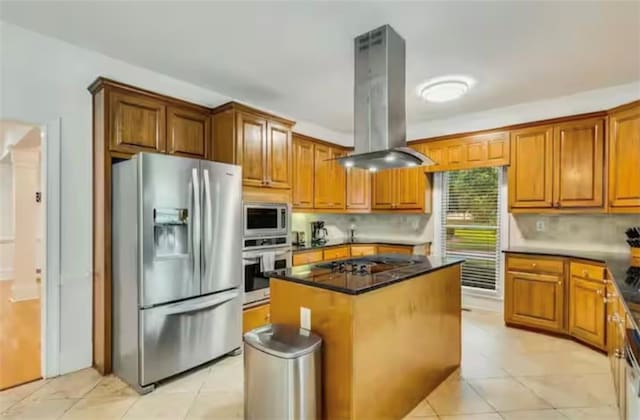 kitchen with island exhaust hood, light tile patterned floors, stainless steel appliances, brown cabinetry, and a kitchen island