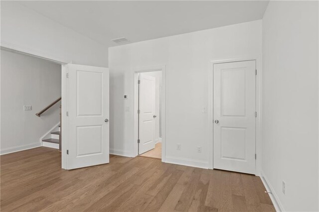 unfurnished bedroom with ensuite bath, visible vents, light wood finished floors, and baseboards