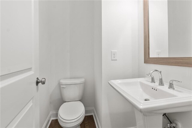 half bath featuring wood finished floors, toilet, baseboards, and a sink
