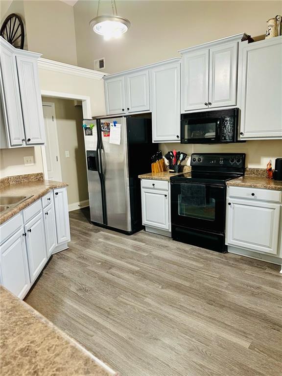 kitchen featuring black appliances, light hardwood / wood-style floors, white cabinets, and a high ceiling