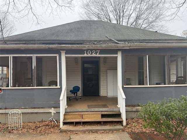 entrance to property featuring a porch and roof with shingles