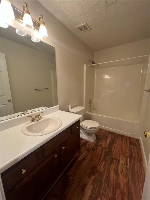 full bathroom featuring shower / bathtub combination, hardwood / wood-style flooring, vanity, toilet, and a textured ceiling