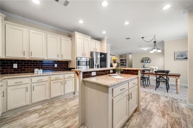 kitchen featuring visible vents, ornamental molding, a center island, light wood-style floors, and appliances with stainless steel finishes