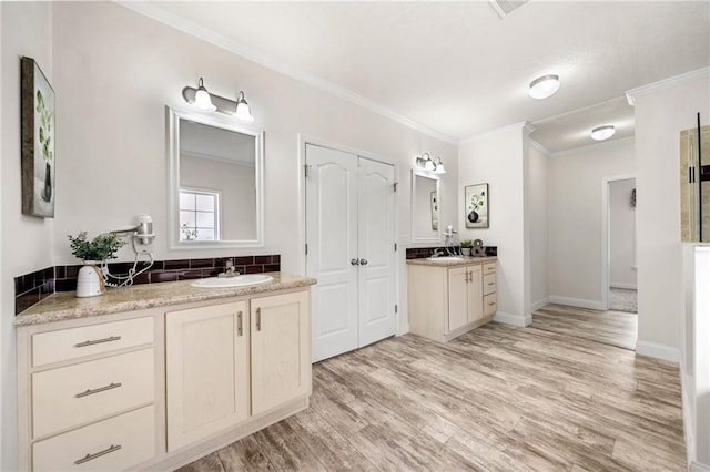 bathroom featuring two vanities, ornamental molding, a sink, wood finished floors, and baseboards