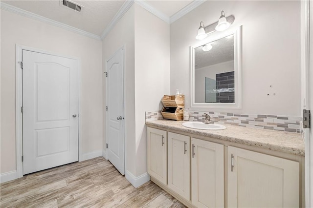 bathroom featuring visible vents, backsplash, wood finished floors, crown molding, and vanity