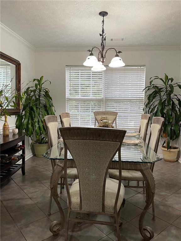 dining area with a textured ceiling, ornamental molding, a notable chandelier, and dark tile patterned floors