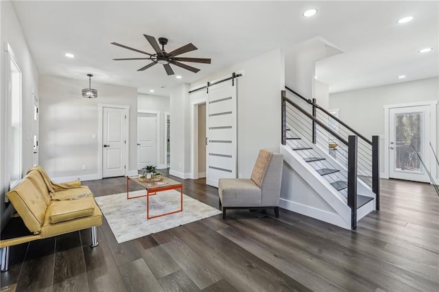 living room featuring dark wood-type flooring, ceiling fan, and a barn door