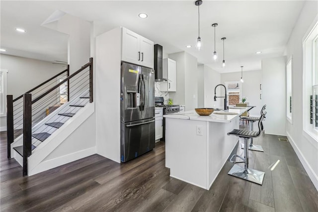 kitchen with appliances with stainless steel finishes, wall chimney range hood, pendant lighting, a breakfast bar, and a kitchen island with sink