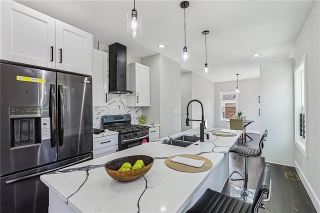 kitchen featuring a center island with sink, stainless steel appliances, light stone counters, white cabinets, and wall chimney range hood