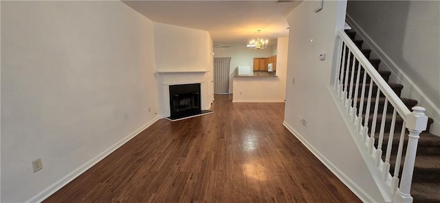 unfurnished living room featuring baseboards, a fireplace with raised hearth, stairs, dark wood-type flooring, and a notable chandelier