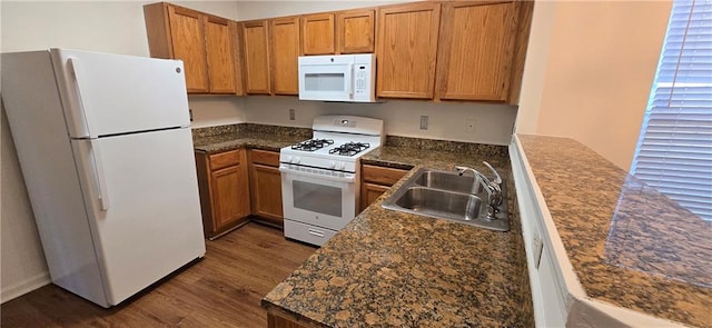 kitchen featuring white appliances, dark wood-style floors, brown cabinetry, a sink, and dark countertops