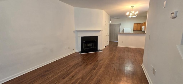 unfurnished living room featuring baseboards, dark wood-type flooring, an inviting chandelier, and a fireplace with raised hearth