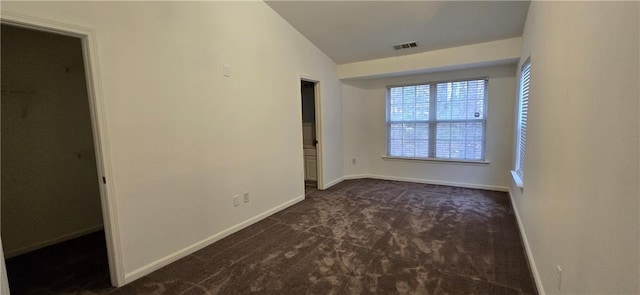 empty room with visible vents, baseboards, lofted ceiling, and dark colored carpet