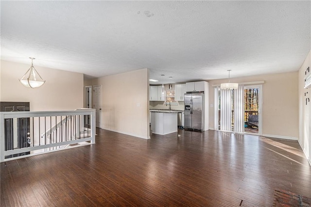 unfurnished living room with a textured ceiling, sink, dark wood-type flooring, and an inviting chandelier