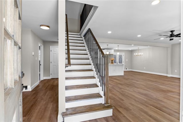 stairway featuring ceiling fan with notable chandelier, baseboards, wood finished floors, and recessed lighting