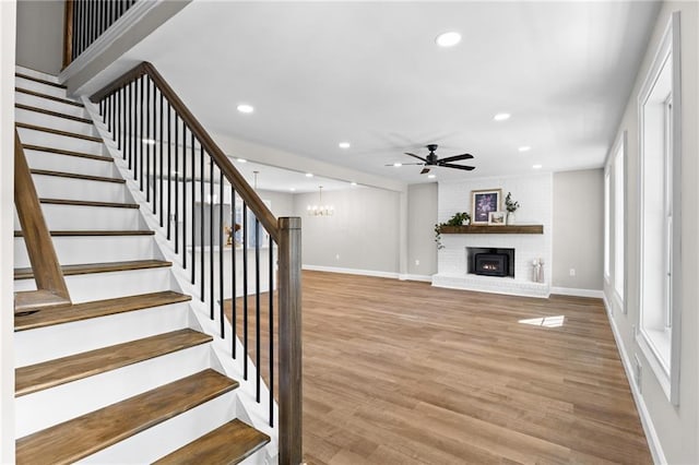 stairway with baseboards, wood finished floors, ceiling fan with notable chandelier, a fireplace, and recessed lighting