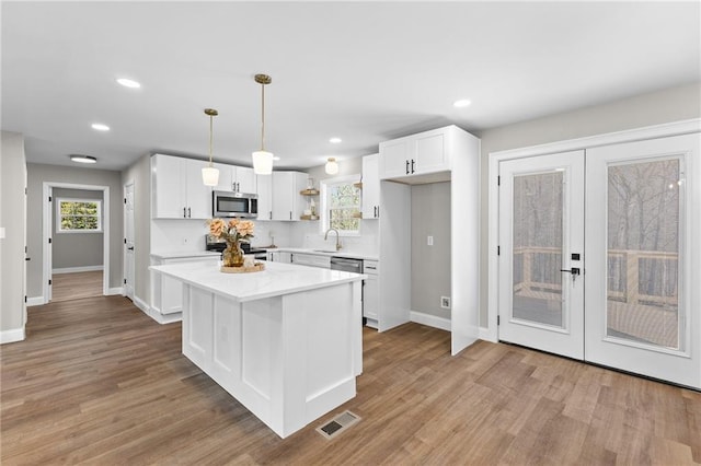 kitchen featuring stainless steel appliances, wood finished floors, a sink, visible vents, and white cabinetry