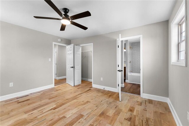 unfurnished bedroom with ceiling fan, connected bathroom, light wood-style flooring, and baseboards