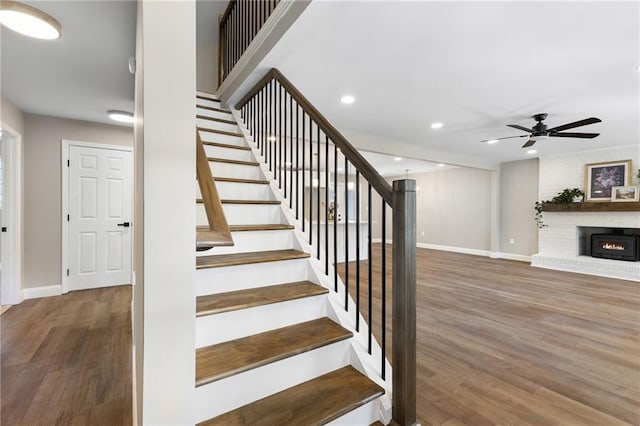 stairway with a ceiling fan, a fireplace, baseboards, and wood finished floors