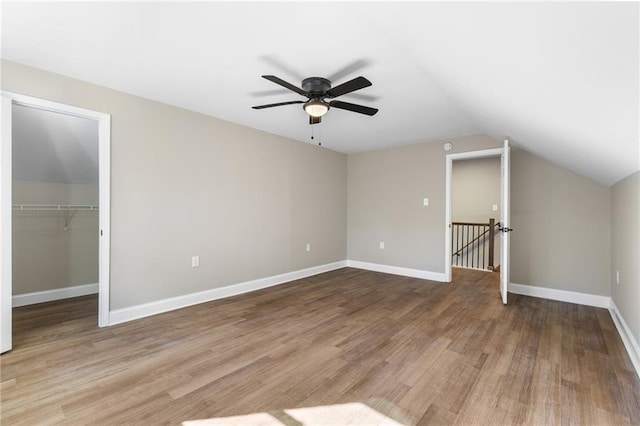 unfurnished bedroom with lofted ceiling, baseboards, a walk in closet, and wood finished floors