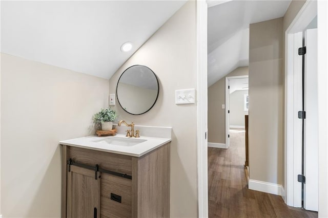 bathroom with vaulted ceiling, wood finished floors, vanity, and baseboards