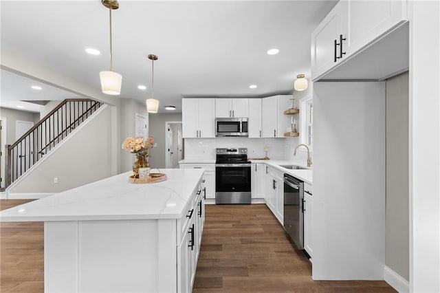 kitchen featuring stainless steel appliances, wood finished floors, a kitchen island, a sink, and decorative backsplash