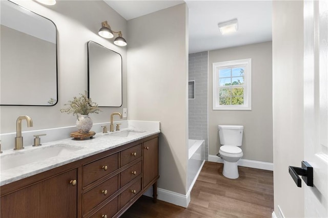 bathroom with double vanity, wood finished floors, a sink, and toilet