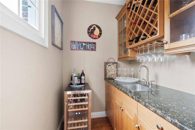 bar with wood-type flooring, sink, beverage cooler, and dark stone counters