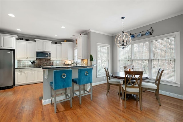 kitchen featuring appliances with stainless steel finishes, pendant lighting, an inviting chandelier, light hardwood / wood-style flooring, and white cabinets