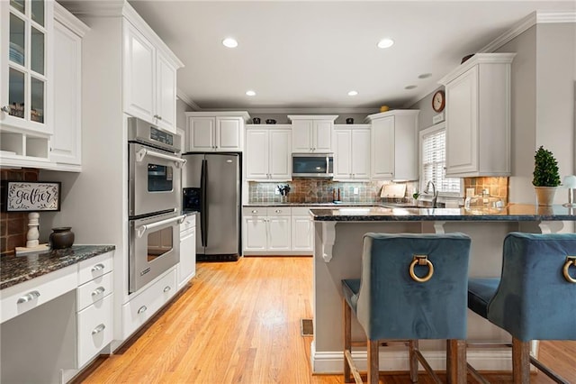 kitchen featuring appliances with stainless steel finishes, a kitchen breakfast bar, crown molding, light hardwood / wood-style flooring, and white cabinets