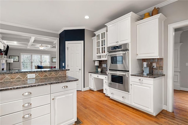 kitchen with light wood-type flooring, tasteful backsplash, stainless steel double oven, ceiling fan, and white cabinets