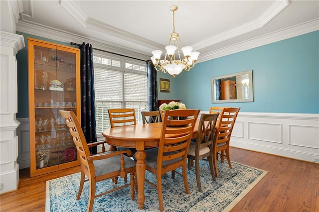 dining space with a raised ceiling, ornamental molding, a notable chandelier, and hardwood / wood-style flooring