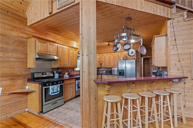 1182 Cedar Rd, Lincolnton, GA 30817 - kitchen featuring stainless steel appliances, under cabinet range hood, wooden walls, dark countertops, and a breakfast bar