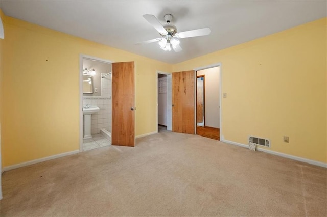 unfurnished bedroom with ensuite bathroom, light colored carpet, and ceiling fan