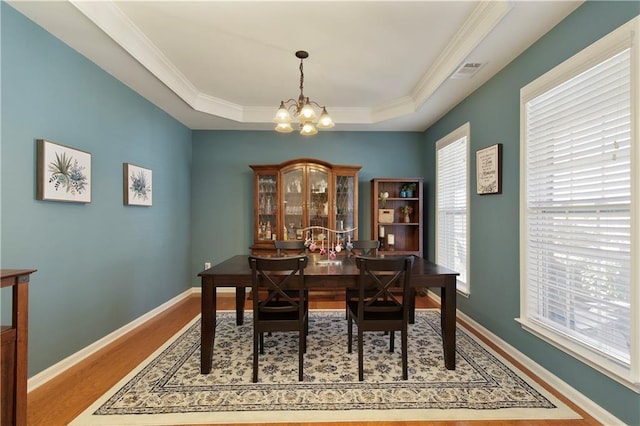 dining space featuring hardwood / wood-style flooring, ornamental molding, a tray ceiling, and a chandelier