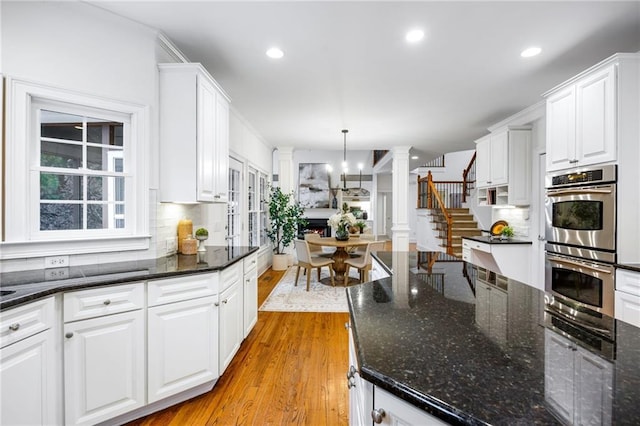 kitchen featuring white cabinetry, decorative light fixtures, dark stone counters, and stainless steel double oven