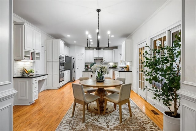 dining area featuring crown molding, a chandelier, and light wood-type flooring