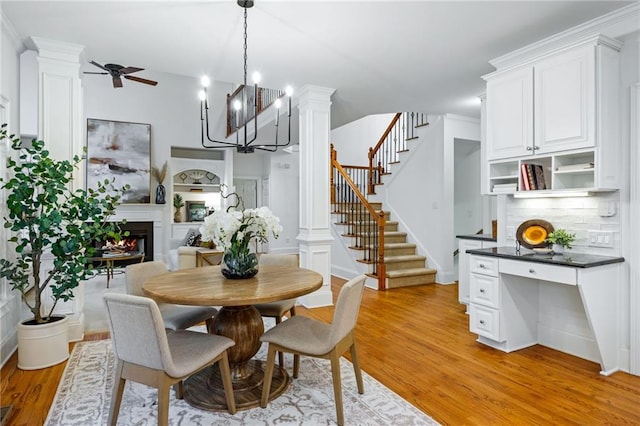 dining room with decorative columns, ceiling fan with notable chandelier, and light wood-type flooring