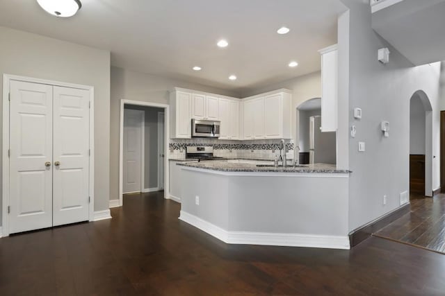 kitchen with light stone counters, arched walkways, dark wood-type flooring, appliances with stainless steel finishes, and white cabinetry