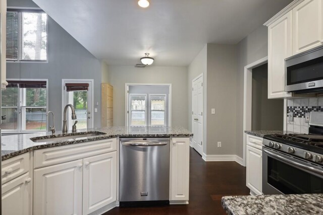 kitchen with tasteful backsplash, dark stone counters, stainless steel appliances, white cabinetry, and a sink