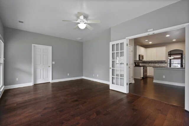 unfurnished living room featuring baseboards, dark wood-style floors, visible vents, and ceiling fan