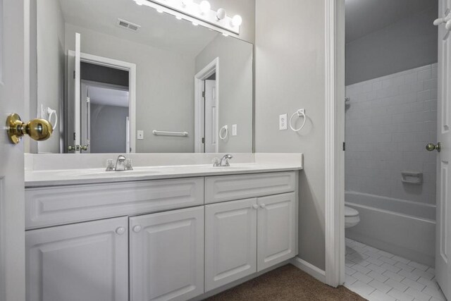 bathroom with double vanity, visible vents, toilet, and a sink