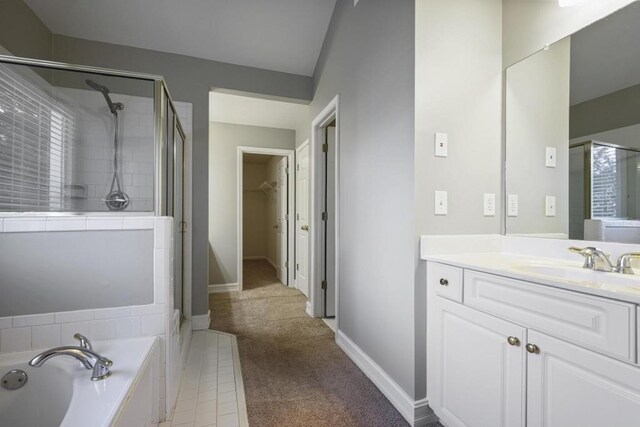 bathroom featuring vanity, baseboards, a shower stall, a walk in closet, and a garden tub