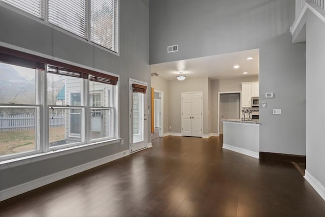 unfurnished living room with visible vents, dark wood-type flooring, recessed lighting, a high ceiling, and baseboards