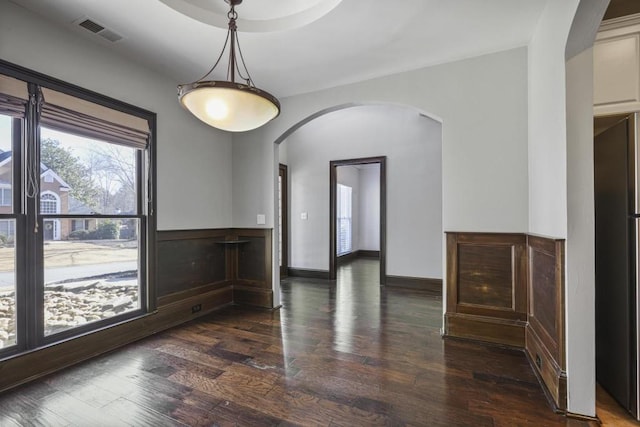 empty room featuring visible vents, arched walkways, baseboards, and wood finished floors