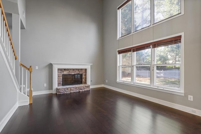 unfurnished living room featuring baseboards, stairs, a fireplace, a high ceiling, and dark wood-style flooring