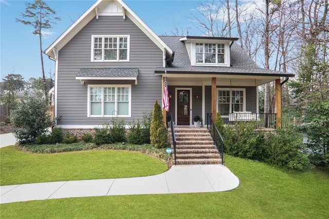 craftsman-style house with covered porch, a front yard, and roof with shingles