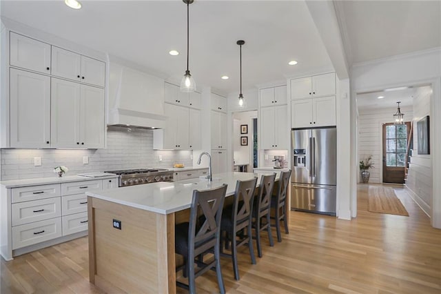 kitchen with light wood-style flooring, high end fridge, custom range hood, range, and backsplash