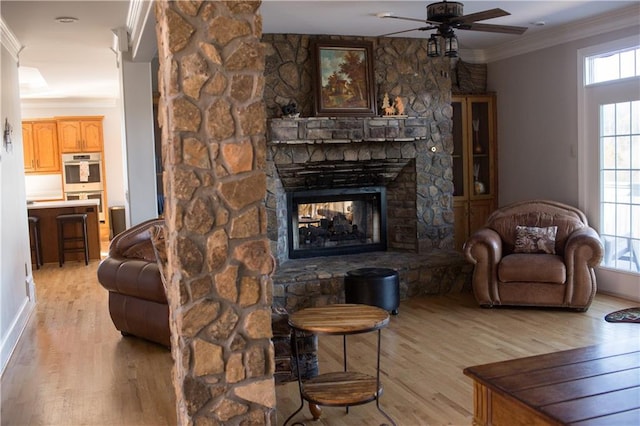 living room with light wood-type flooring, a stone fireplace, ceiling fan, and crown molding