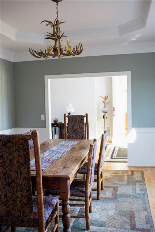 dining room featuring a tray ceiling, wood-type flooring, a notable chandelier, and ornamental molding